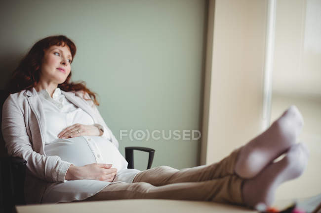 Беременная деловая женщина отдыхает с поднятыми ногами в офисе — стоковое фото