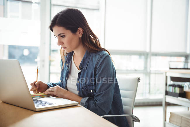 Business executive looking at laptop and writing on sticky notes in office — Stock Photo