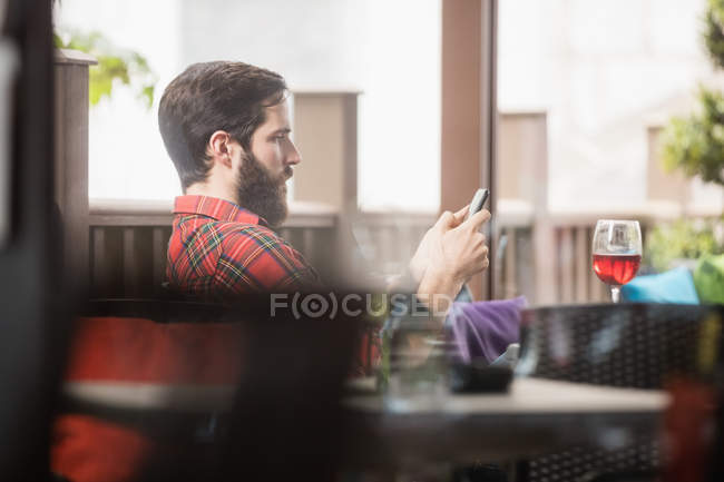 Homem usando telefone celular com copo de vinho na mesa no bar — Fotografia de Stock