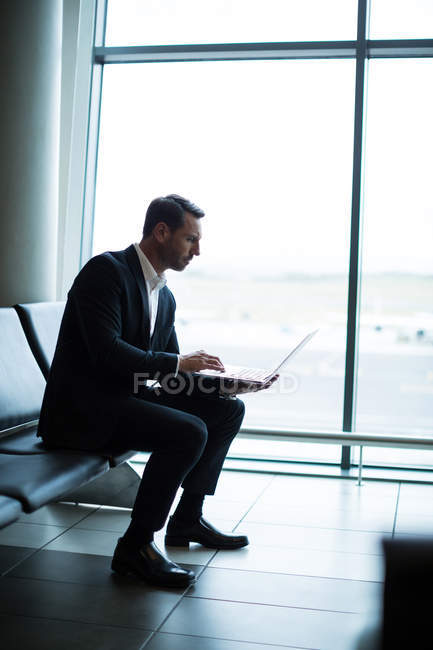 Empresario que usa laptop en la sala de espera en la terminal del aeropuerto - foto de stock