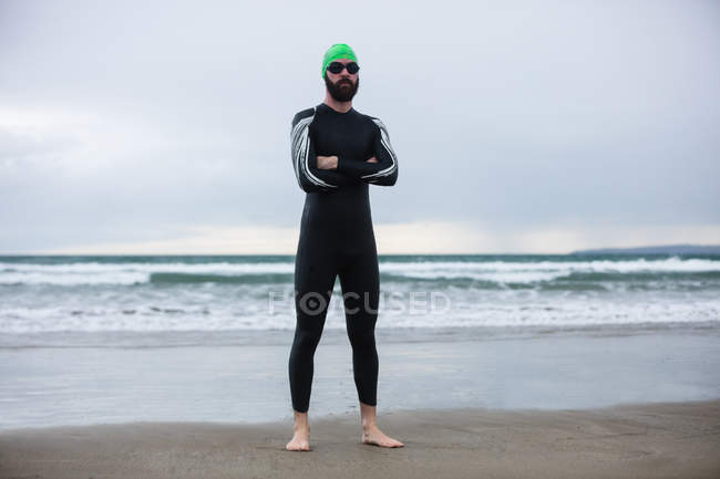 Retrato de atleta de terno molhado de pé com as mãos cruzadas na praia — Fotografia de Stock