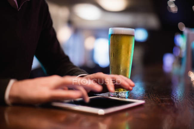 Man using digital tablet with glass of beer on counter in bar — Stock Photo