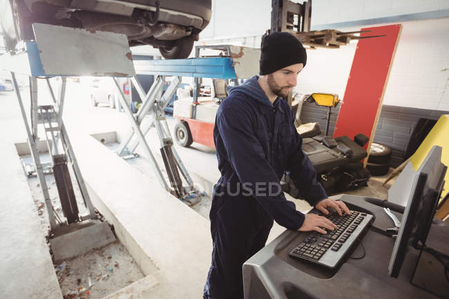 Mecânico de trabalho em computador pessoal na garagem de reparação — Fotografia de Stock
