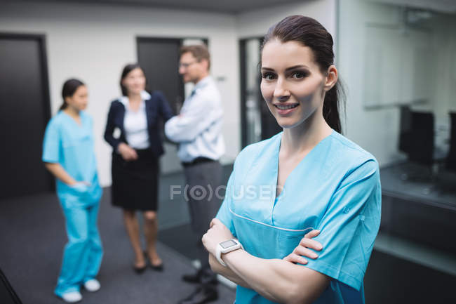 Portrait of smiling nurse standing with arms crossed in hospital corridor — Stock Photo