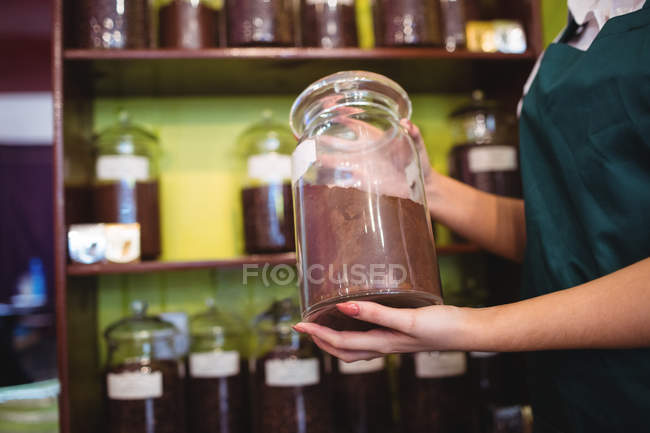Mid section of female shopkeeper holding jar of spices in shop — Stock Photo