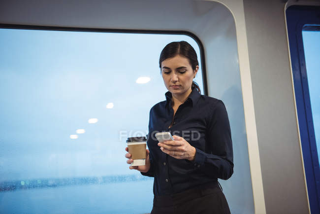 Mulher de negócios bonita com xícara de café usando telefone enquanto está de pé no trem — Fotografia de Stock