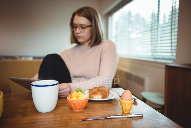 Woman using digital tablet while having breakfast in living room at home — Stock Photo