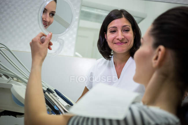 Пациентка проверяет зубы в зеркале в стоматологической клинике — стоковое фото