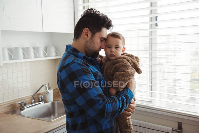 Father holding baby boy while standing in kitchen — Stock Photo