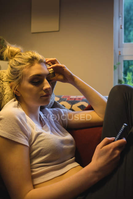 Женщина лежит и использует мобильный телефон на диване в гостиной на дому — стоковое фото