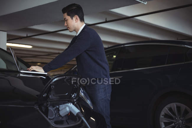 Mann benutzt Laptop beim Laden von Elektroauto in Garage — Stockfoto