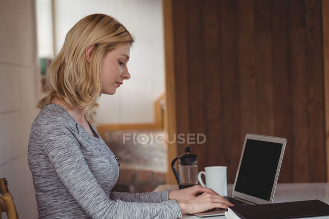 Красива жінка сидить за столом і використовує ноутбук вдома — стокове фото