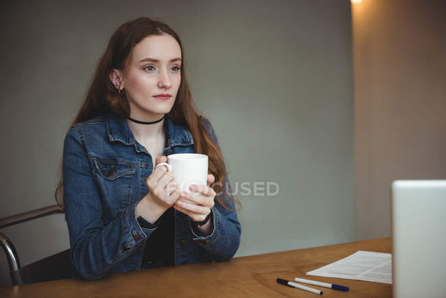 Thoughtful woman having cup of coffee in office — Stock Photo