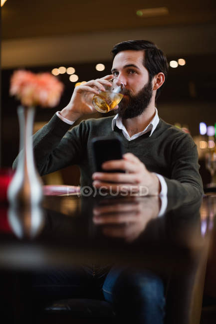 Uomo che tiene il cellulare e beve qualcosa al bar — Foto stock