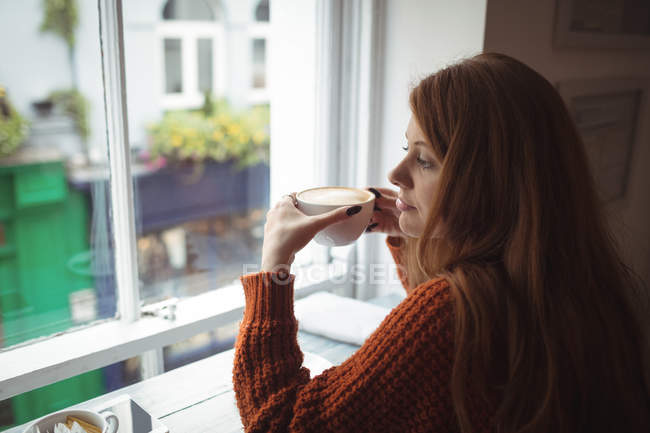Mujer joven tomando café en la ventana del restaurante - foto de stock