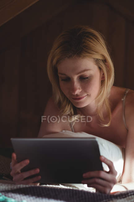 Женщина лежит на кровати и пользуется цифровым планшетом в спальне дома — стоковое фото