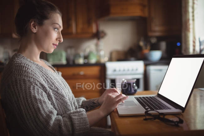 Женщина использует ноутбук на столе на кухне дома — стоковое фото