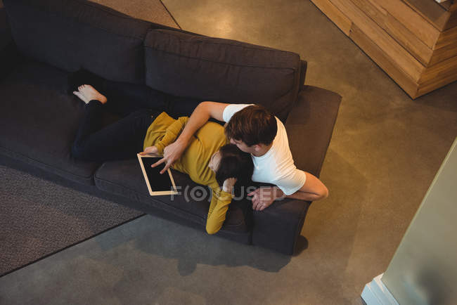 Casal alegre deitado juntos no sofá usando tablet digital na sala de estar — Fotografia de Stock