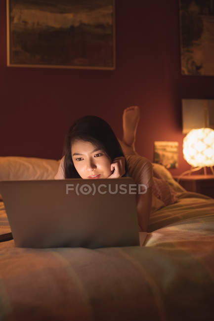 Frau liegt und benutzt Laptop auf Bett im Schlafzimmer — Stockfoto
