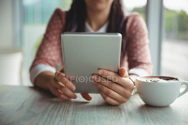 Mid section of woman using digital tablet while having cup of coffee cafe — Stock Photo