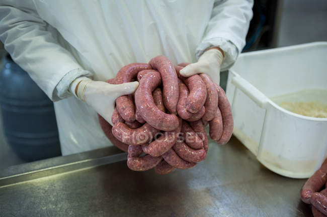 Milieu de la boucherie détenant des saucisses crues dans une usine de viande — Photo de stock