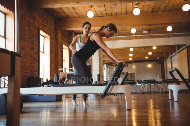 Entrenador ayudando a una mujer mientras practica pilates en un gimnasio - foto de stock