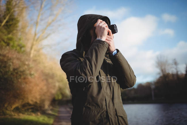 Hombre tomando fotos con la cámara cerca de la orilla del río - foto de stock