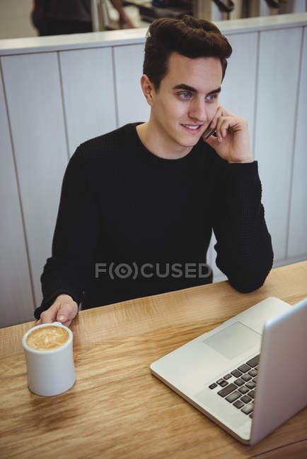 Homem falando no celular enquanto toma café na cafeteria — Fotografia de Stock