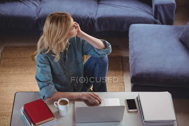 Nachdenkliche Frau benutzt Laptop im heimischen Wohnzimmer — Stockfoto