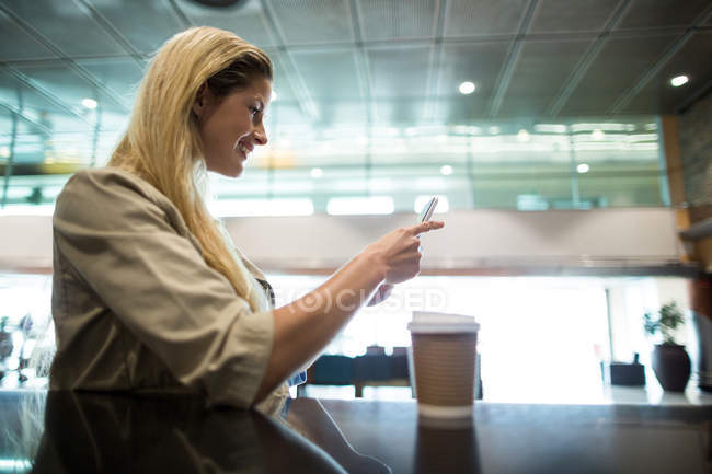 Mulher sorridente usando telefone celular na área de espera no terminal do aeroporto — Fotografia de Stock