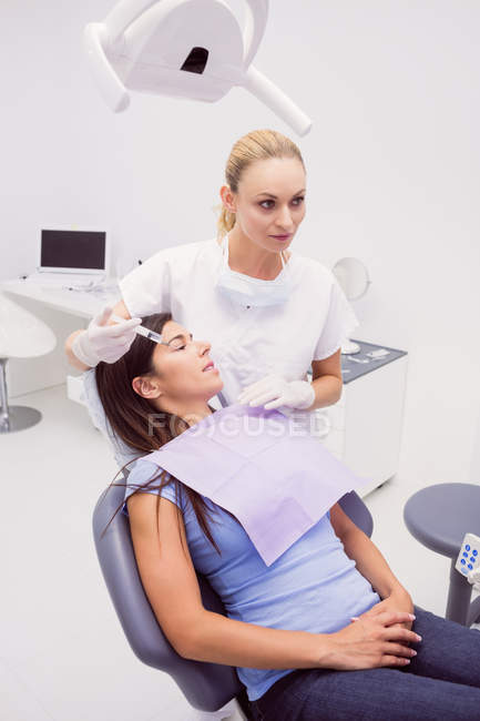 Dentista sosteniendo jeringa mientras examina al paciente en la clínica - foto de stock