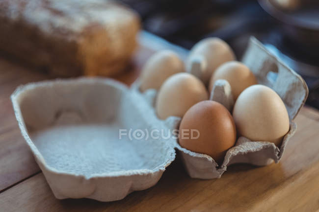 Primer plano de huevos en cartón de huevo sobre mesa de madera - foto de stock