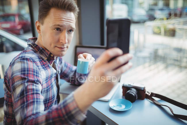 Young man taking selfie on mobile phone in cafeteria — Stock Photo