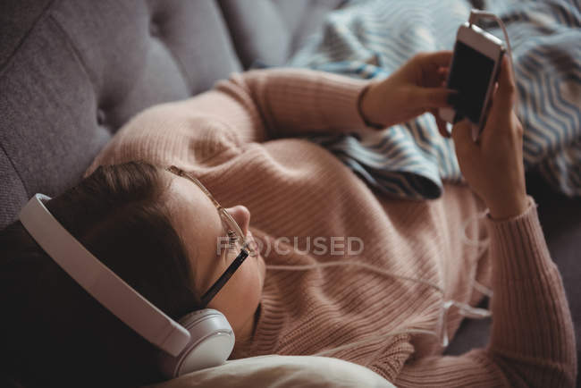 Женщина лежит на диване и слушает музыку на мобильном телефоне в гостиной дома — стоковое фото