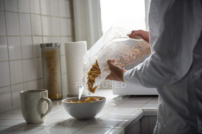 Серединний розріз людини, що поливає зернові в мисці в домашніх умовах — стокове фото