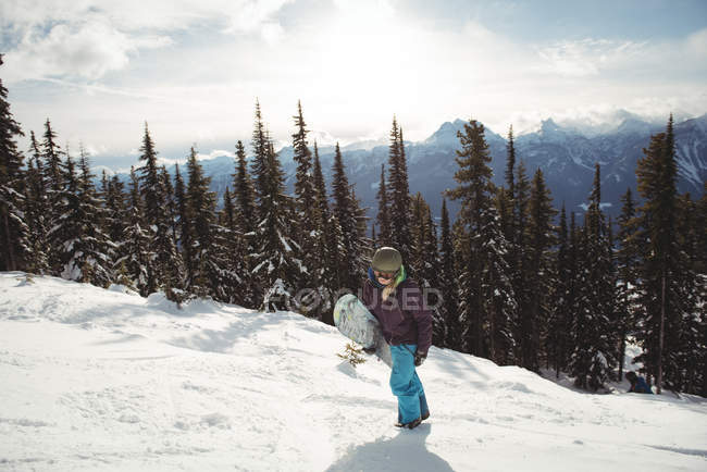 Woman holding snowboard on mountain against trees during winter — Stock Photo