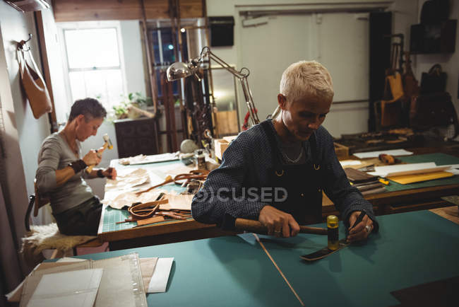 Madura artesana martillando cuero en taller - foto de stock