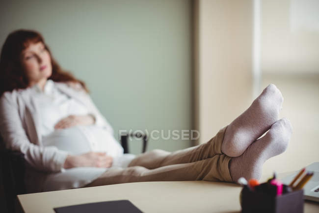 Беременная деловая женщина отдыхает с поднятыми ногами в офисе — стоковое фото