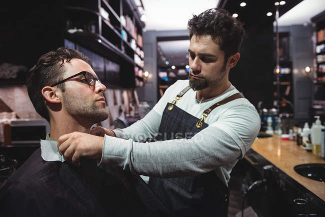 Barbiere mettere mantello sopra cliente in negozio di barbiere — Foto stock