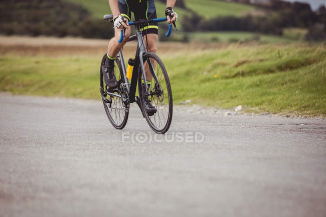 Low section of athlete riding bicycle on country road — Stock Photo