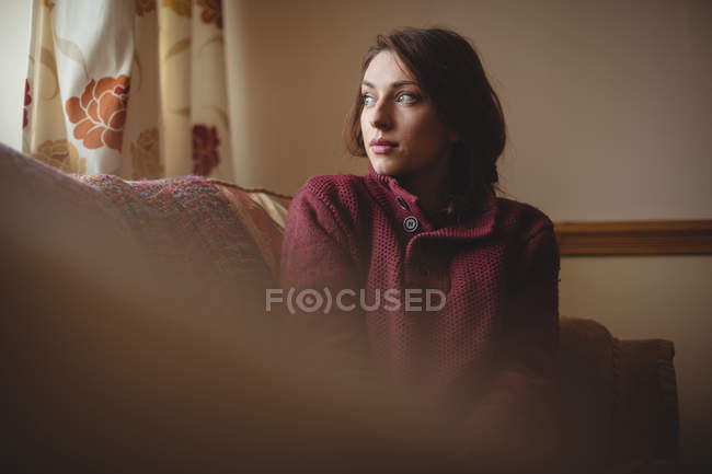 Mujer pensativa sentada en el sofá en la sala de estar en casa - foto de stock