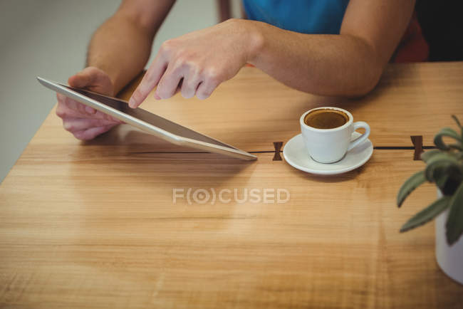 Руки человека с помощью цифровой таблетки с чашкой кофе на столе в кафе — стоковое фото
