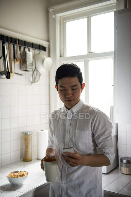 Человек, использующий мобильный телефон во время чашки кофе дома — стоковое фото