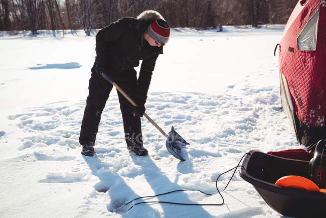 Eisfischer gräbt mit Schaufel in verschneiter Landschaft — Stockfoto