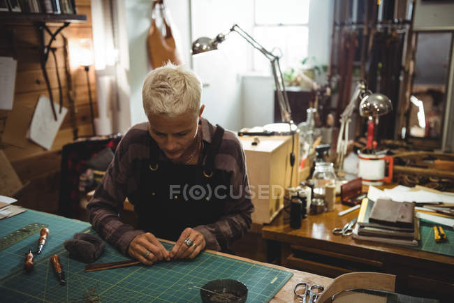 Aufmerksame Handwerkerin schneidet in Werkstatt ein Stück Leder — Stockfoto