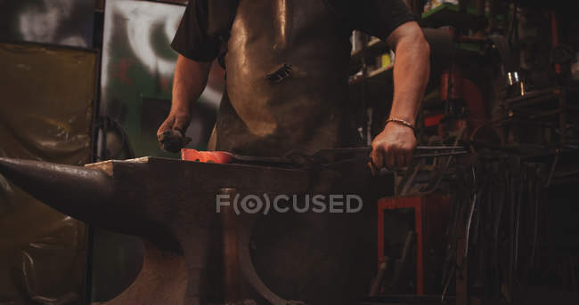 Schmied im mittleren Abschnitt bearbeitet heißes Metall mit Hammer in der Werkstatt — Stockfoto