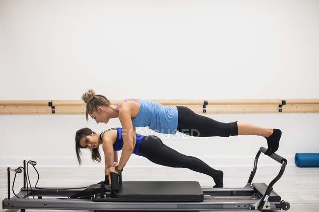 Female trainer assisting woman with stretching exercise on reformer in gym — Stock Photo