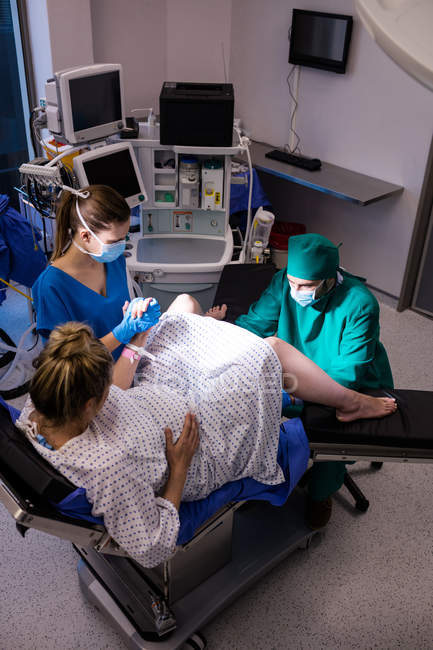 Медицинская команда, осматривающая беременную женщину во время родов в операционной — стоковое фото