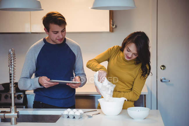 Coppia utilizzando tablet digitale durante la preparazione dei cookie in cucina a casa — Foto stock