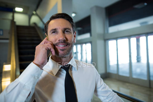 Businessman on escalator talking on mobile phone in airport — Stock Photo